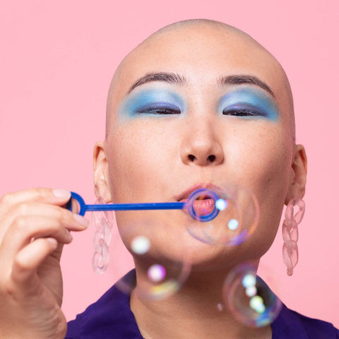 hair loss cancer patient blowing bubbles wearing eye care dermo-cosmetics